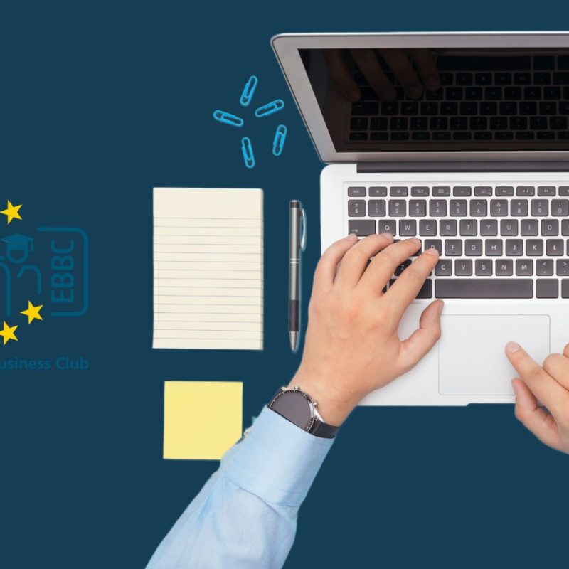 Top-down view of a workspace with hands typing on a laptop keyboard, next to a notepad, pen, and a spiral notebook, all on a dark blue background. In the top left corner is the logo of the European Battery Business Club (EBBC), symbolizing a network focused on battery business and training.