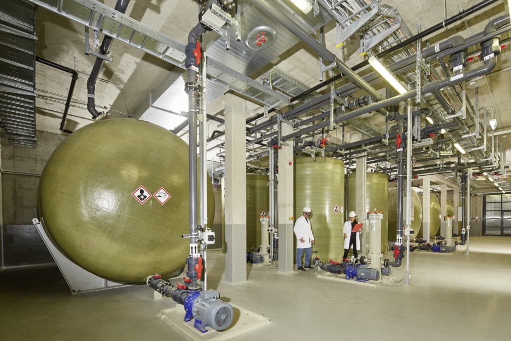 green-gray tanks about double the height of a human in an industrial style hall