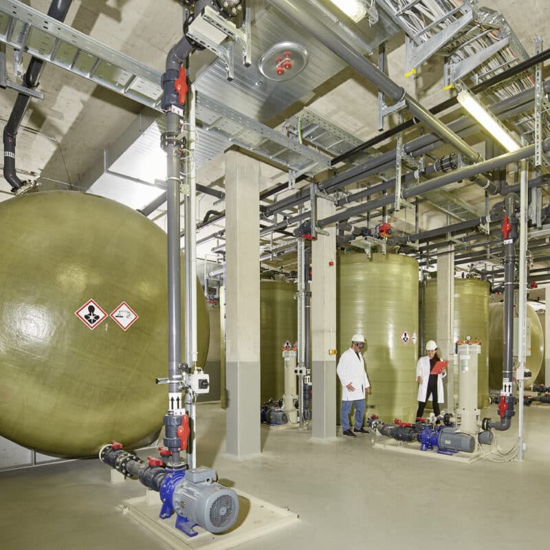 green-gray tanks about double the height of a human in an industrial style hall
