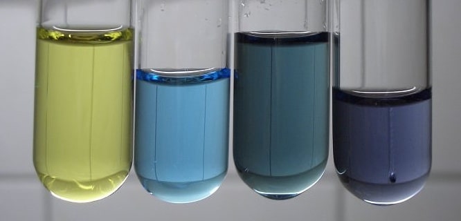 there are four vials filled with solutions of different colours. from left to right: yellow, light blue, dark-grayisch blue, violet.